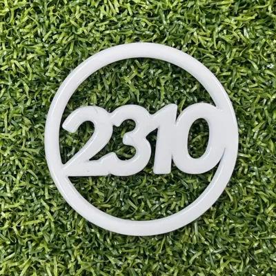 緑の芝生の上に置かれた、数字の「2310」がデザインされた白色の円形ロゴプレート